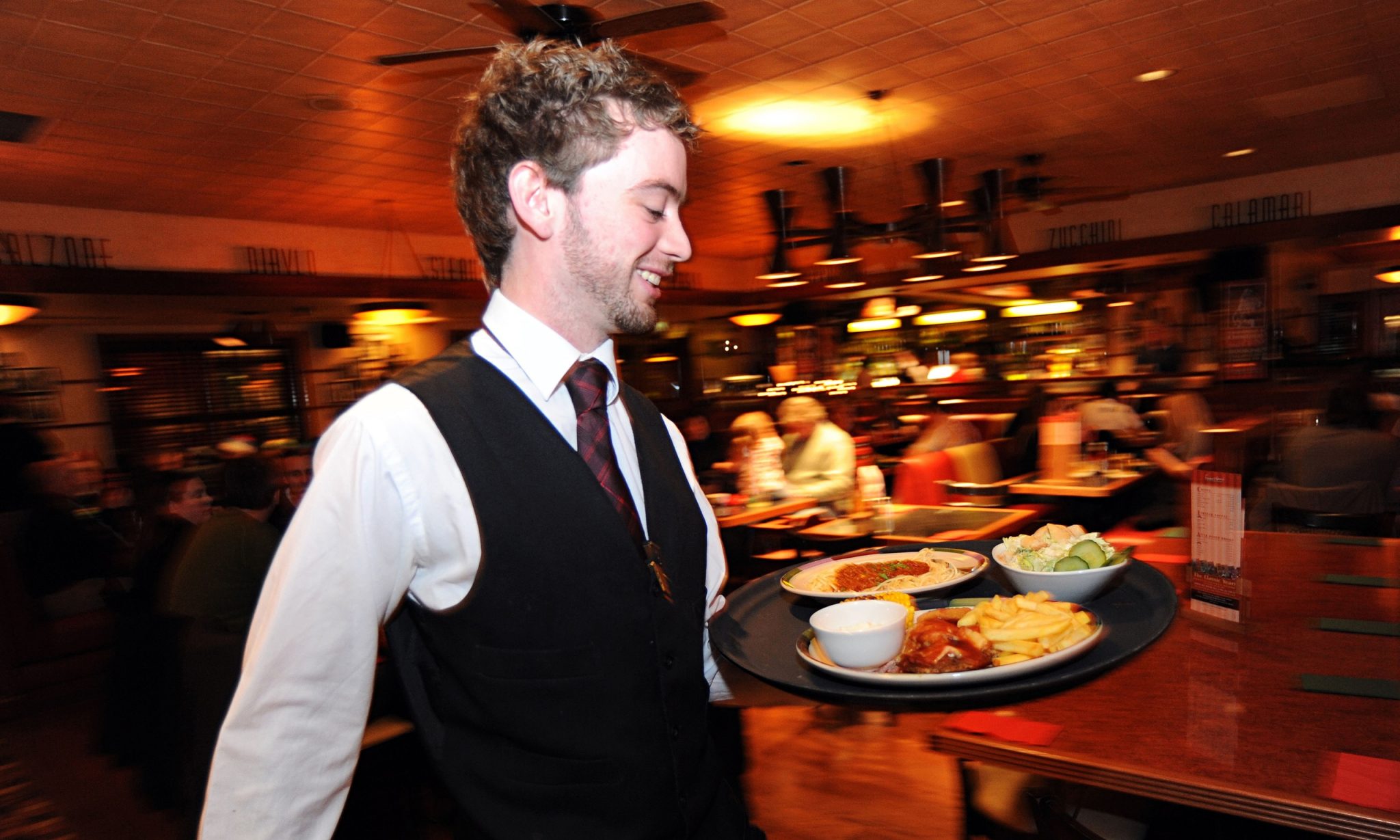 A waiter rushes with a tray of food in a busy restaurant Bradford West
